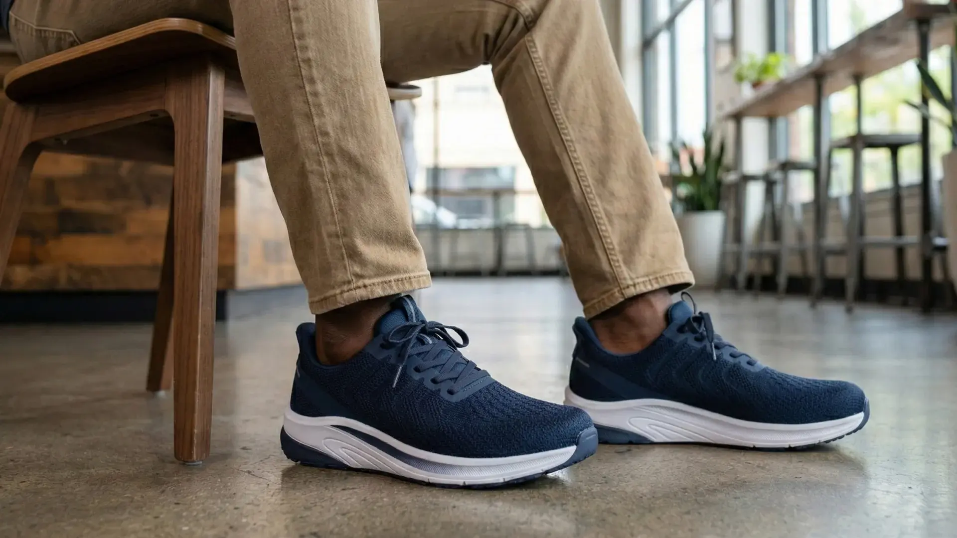 Mann in Chinos mit marineblauen Orthofeet-Sneakern in einem hellen Café