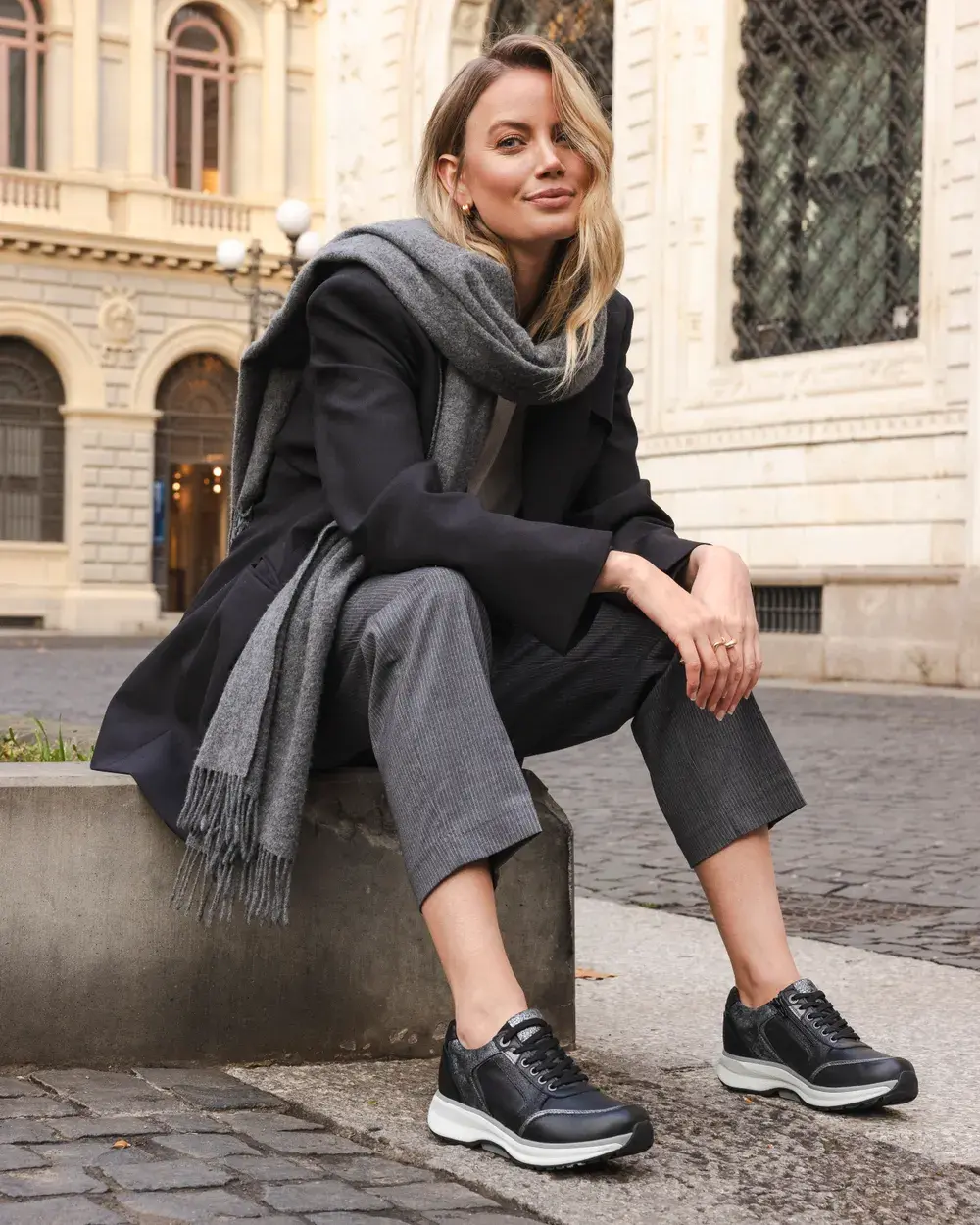 Frau sitzt auf einer Mauer in einer Altstadtgasse und trägt schwarze Sneaker mit heller Sohle