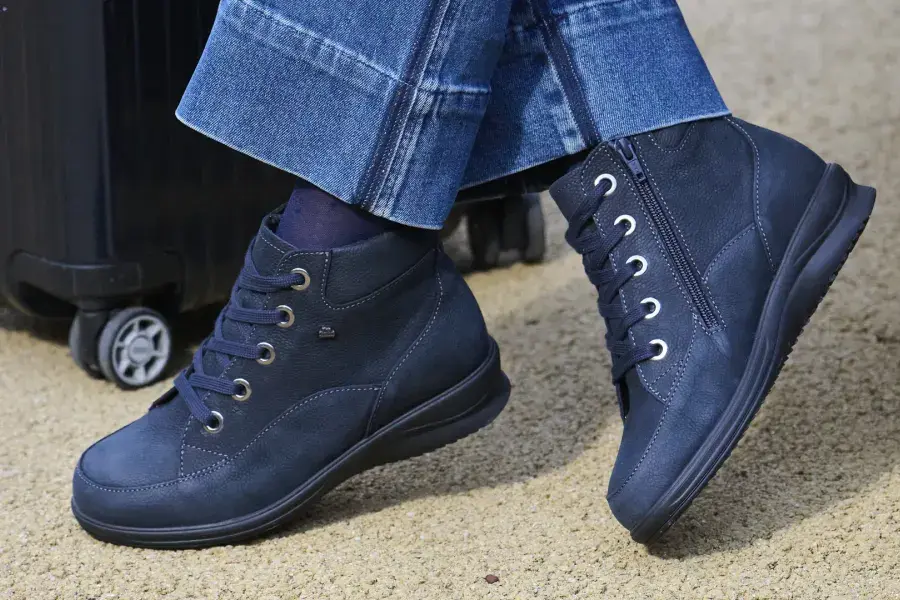 Blaue Schnürstiefeletten mit Reißverschluss neben einem Rollkoffer