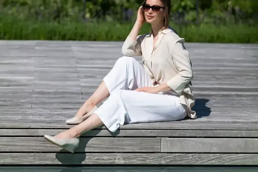 Frau in weißer Leinenhose sitzt mit Slingpumps auf einem Holzsteg