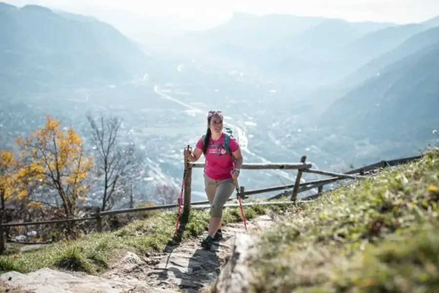 Wanderin mit Stöcken auf einem Bergpfad über dem Tal