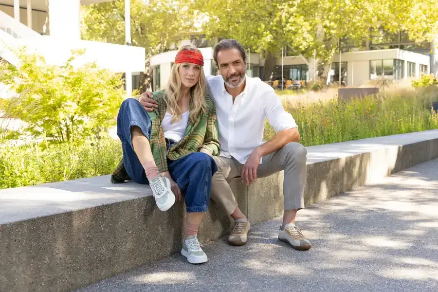 Paar sitzt mit Sneakern auf einer Mauer im Grünen