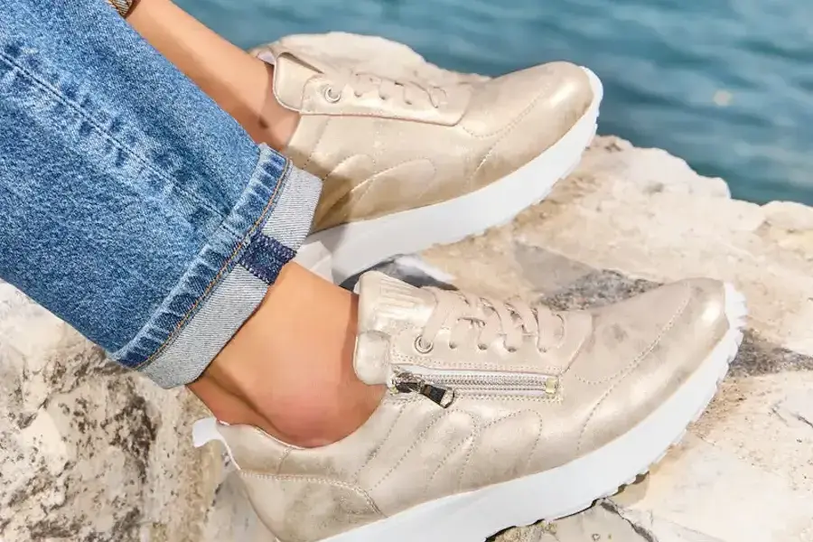 Goldfarbene Sneaker mit Reißverschluss auf einem Felsen am See